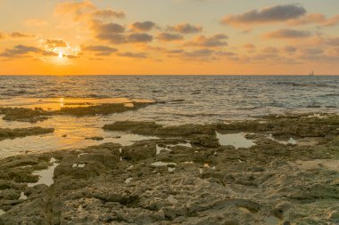 Akdeniz kıyılarının gün batımı manzarası, aşınma platformları ve bir yelkenli, Shikmona Park, Hayfa, İsrail