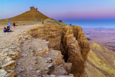 Mitzpe Ramon, İsrail - 10 Ağustos 2021: Güney İsrail 'deki Negev Çölü' nde, Makhtesh (krater) Ramon 'un kıyısında ziyaretçilerle gün batımı manzarası