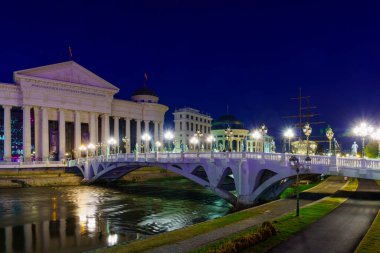 Üsküp, Kuzey Makedonya - 04 Ekim 2023: Üsküp, Kuzey Makedonya 'daki Vardar Nehri ve Medeniyetler Köprüsü' nün akşam manzarası