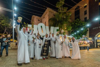 Hayfa, İsrail - 31 Aralık 2025: Katar Şeyhi gibi giyinmiş bir grup aktivist, Katar-kapısı yolsuzluk olayının sembolik bir protestosu olarak insanlara para dağıtıyor. Alman Kolonisi, Hayfa, İsrail