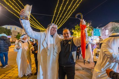 Hayfa, İsrail - 31 Aralık 2025: Katar Şeyhi gibi giyinmiş bir grup aktivist, Katar-kapısı yolsuzluk olayının sembolik bir protestosu olarak insanlara para dağıtıyor. Alman Kolonisi, Hayfa, İsrail