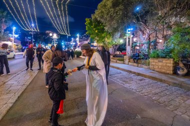 Hayfa, İsrail - 31 Aralık 2025: Katar Şeyhi gibi giyinmiş bir grup aktivist, Katar-kapısı yolsuzluk olayının sembolik bir protestosu olarak insanlara para dağıtıyor. Alman Kolonisi, Hayfa, İsrail