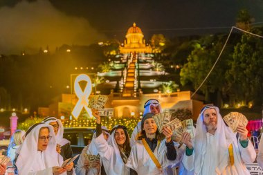 Hayfa, İsrail - 31 Aralık 2025: Katar Şeyhi gibi giyinmiş bir grup aktivist, Katar-kapısı yolsuzluk olayının sembolik bir protestosu olarak insanlara para dağıtıyor. Alman Kolonisi, Hayfa, İsrail