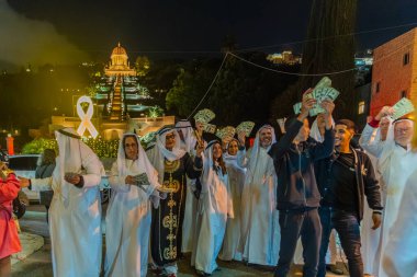 Hayfa, İsrail - 31 Aralık 2025: Katar Şeyhi gibi giyinmiş bir grup aktivist, Katar-kapısı yolsuzluk olayının sembolik bir protestosu olarak insanlara para dağıtıyor. Alman Kolonisi, Hayfa, İsrail