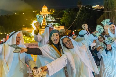 Hayfa, İsrail - 31 Aralık 2025: Katar Şeyhi gibi giyinmiş bir grup aktivist, Katar-kapısı yolsuzluk olayının sembolik bir protestosu olarak insanlara para dağıtıyor. Alman Kolonisi, Hayfa, İsrail