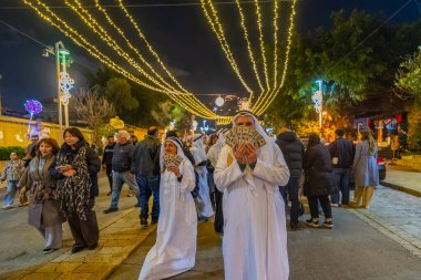 Hayfa, İsrail - 31 Aralık 2025: Katar Şeyhi gibi giyinmiş bir grup aktivist, Katar-kapısı yolsuzluk olayının sembolik bir protestosu olarak insanlara para dağıtıyor. Alman Kolonisi, Hayfa, İsrail