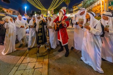 Hayfa, İsrail - 31 Aralık 2025: Katar Şeyhi gibi giyinmiş bir grup aktivist, Katar-kapısı yolsuzluk olayının sembolik bir protestosu olarak insanlara para dağıtıyor. Alman Kolonisi, Hayfa, İsrail
