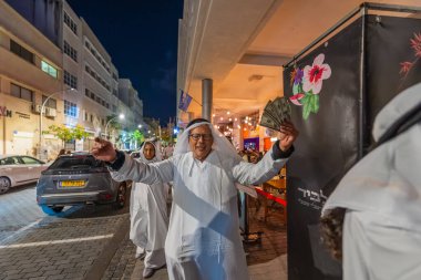 Hayfa, İsrail - 31 Aralık 2025: Katar Şeyhi gibi giyinmiş bir grup aktivist, Katar-kapısı yolsuzluk olayının sembolik bir protestosu olarak insanlara para dağıtıyor. Şehir merkezi, Hayfa, İsrail
