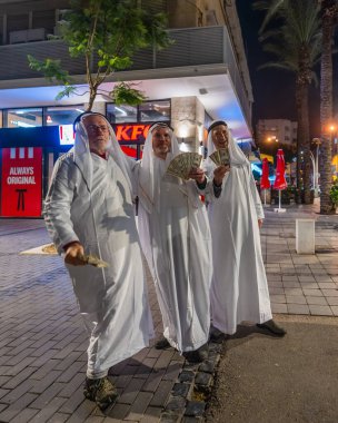 Hayfa, İsrail - 31 Aralık 2025: Katar Şeyhi gibi giyinmiş bir grup aktivist, Katar-kapısı yolsuzluk olayının sembolik bir protestosu olarak insanlara para dağıtıyor. Şehir merkezi, Hayfa, İsrail