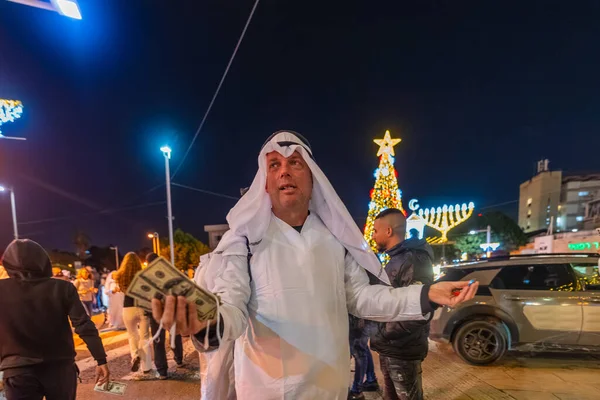 Hayfa, İsrail - 31 Aralık 2025: Katar Şeyhi gibi giyinmiş bir grup aktivist, Katar-kapısı yolsuzluk olayının sembolik bir protestosu olarak insanlara para dağıtıyor. Alman Kolonisi, Hayfa, İsrail