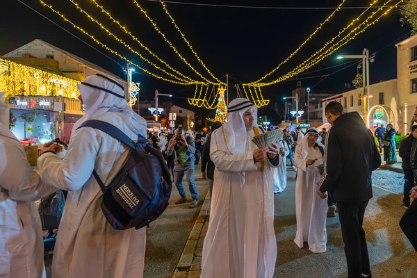 Hayfa, İsrail - 31 Aralık 2025: Katar Şeyhi gibi giyinmiş bir grup aktivist, Katar-kapısı yolsuzluk olayının sembolik bir protestosu olarak insanlara para dağıtıyor. Alman Kolonisi, Hayfa, İsrail