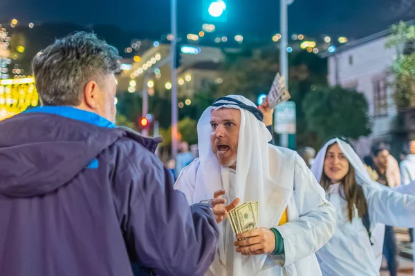 Hayfa, İsrail - 31 Aralık 2025: Katar Şeyhi gibi giyinmiş bir grup aktivist, Katar-kapısı yolsuzluk olayının sembolik bir protestosu olarak insanlara para dağıtıyor. Alman Kolonisi, Hayfa, İsrail