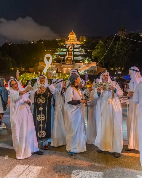 Hayfa, İsrail - 31 Aralık 2025: Katar Şeyhi gibi giyinmiş bir grup aktivist, Katar-kapısı yolsuzluk olayının sembolik bir protestosu olarak insanlara para dağıtıyor. Alman Kolonisi, Hayfa, İsrail