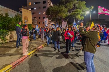 Hayfa, İsrail - 24 Ocak 2026: Çeşitli tabelaları ve bayrakları olan insanlar, hükümete karşı düzenlenen bir protesto mitingine katıldı, yeni polis gereksinimleri nedeniyle kaldırıma itildi. Hayfa, İsrail