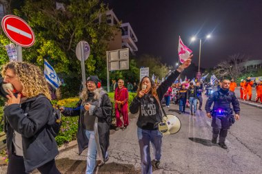 Hayfa, İsrail - 24 Ocak 2026: Çeşitli tabelaları ve bayrakları olan insanlar, hükümete karşı düzenlenen bir protesto mitingine katıldı, yeni polis gereksinimleri nedeniyle kaldırıma itildi. Hayfa, İsrail
