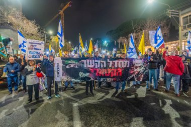 Hayfa, İsrail - 24 Ocak 2026: Çeşitli tabelaları ve bayrakları olan insanlar, hükümete karşı düzenlenen bir protesto mitingine katıldı, yeni polis gereksinimleri nedeniyle kaldırıma itildi. Hayfa, İsrail