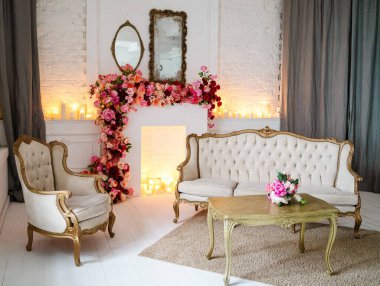 Klasik kanepe, sandalye, mumlu masa. Çiçeklerle süslenmiş şömine..