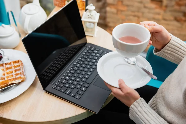 女の子はノートパソコン付きのテーブルでカフェでお茶を飲んでいます — ストック写真