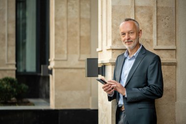 Gri takım elbiseli, akıllı telefonlu gülümseyen bir işadamı..