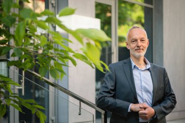 Gri takım elbiseli adam korkuluklara yaslandı..