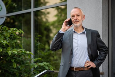 Gri takım elbiseli, akıllı telefonlu gülümseyen bir işadamı..