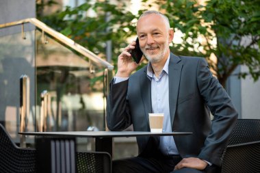 Gri takım elbiseli, akıllı telefonlu gülümseyen bir işadamı..