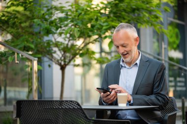 Gri takım elbiseli, akıllı telefonlu gülümseyen bir işadamı..