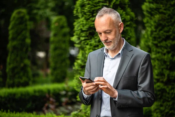 Smiling businessman in a gray suit with a smartphone.