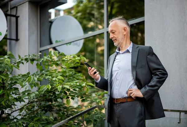Gri takım elbiseli, akıllı telefonlu gülümseyen bir işadamı..