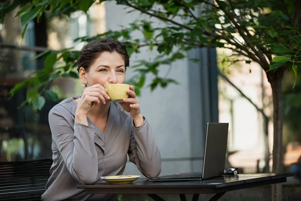 Beautiful business woman is drinking coffee at a table in an outdoor restaurant.