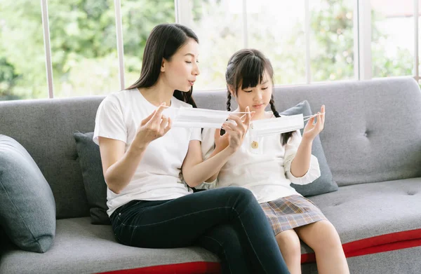 Young Asian mother and little daughter using medical protective mask to health protection and prevention from flu virus, epidemic , infectious diseases and covid-19. Caring for loved ones concept.