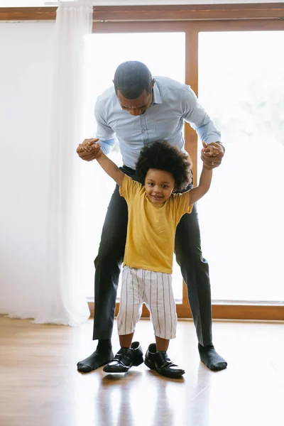 Funny Time.Happy African American father carry little son into the house while the child was playing on his father\'s shoes after work. Welcome back home daddy or family reunion concept.