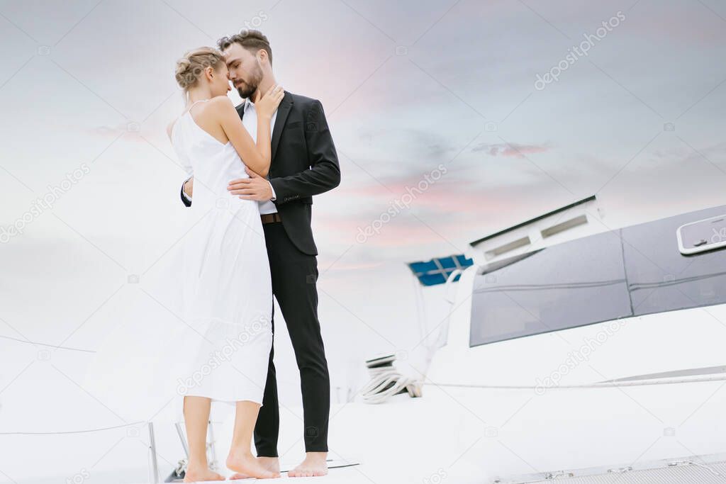 Portrait of young caucasian couple in love relaxing on luxury yacht in the sea. People celebrating wedding anniversary on boat trip. Love relationship and travel lifestyle concept.