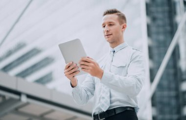 Ofis binasının yanında duran dijital tablette yakışıklı bir işadamı. Mobil teknoloji ve iletişim kavramı.