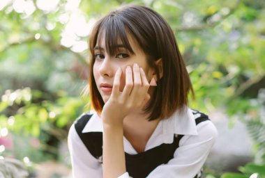 Taş sınırında oturan ve Sunny Park 'taki kameraya bakan genç Asyalı kadının yakın plan portresi. Tatil etkinliği ve yaşam tarzı konsepti.