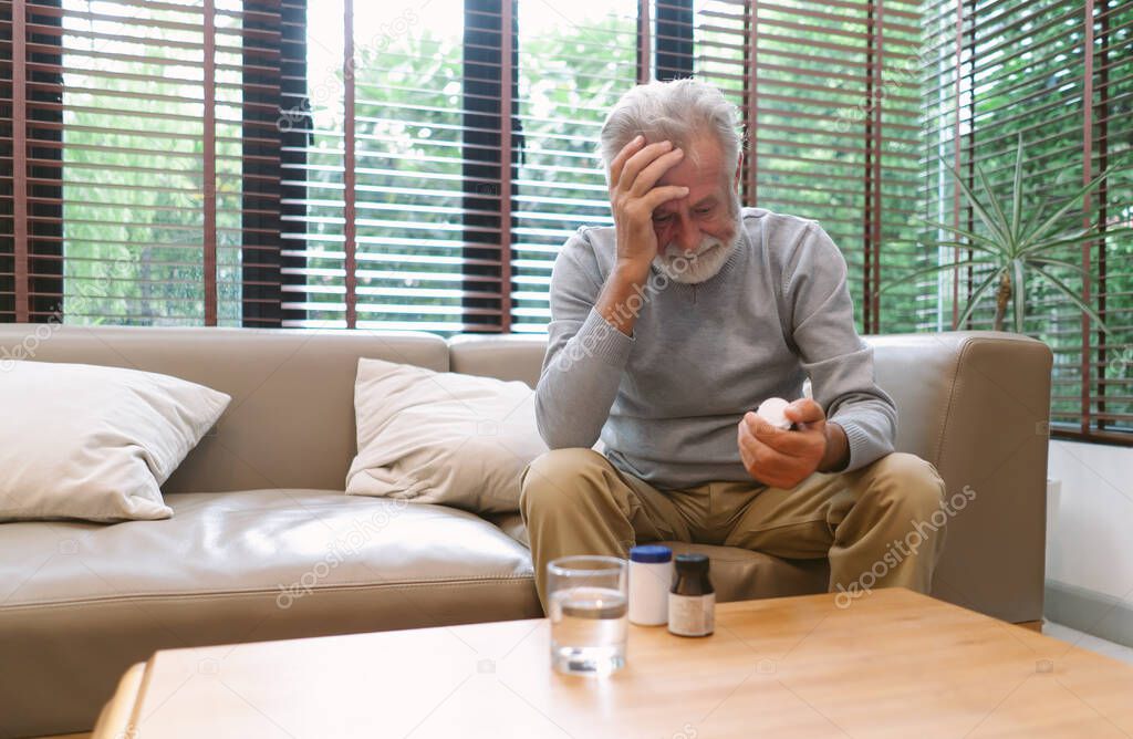 Portrait of a sick elderly man feeling sick ill suffering from headache. He taking antibiotic antidepressant painkiller pill medication to relieve pain at home. Elderly healthcare concept.