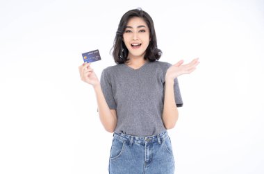 Happy excited amazed young Asian woman in grey t-shirt and jeans holding bank card holding credit card on isolated over white background.