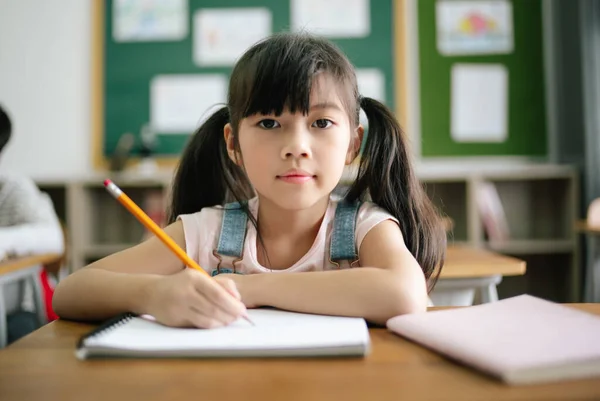 Portrait Little Asian Girl Writing Drawing Notebook Desk Classroom Looking — Stock Photo, Image