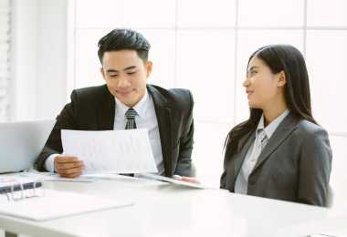 Asyalı işadamı ve işkadını iş belgelerini konuşuyor ve okuyor ve ofiste buluşurken gülümsüyor..