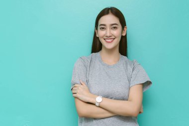 Uzun saçlı mutlu Asyalı kadın gündelik gri gömlek giyiyor. Kollarını turkuaz arka planda kavuşturuyor. Güven pozitifliğini, profesyonelliği ve fotokopi alanı olan modern yaşam tarzını ifade ediyor..