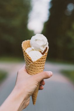 Elde dondurma. Yeşil ağaçların arka planında vanilyalı dondurma ile Macro shot. Lezzetli ve lezzetli tatlı..