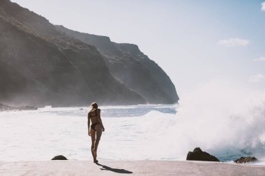 Okyanusun kenarında duran bir kız. Güzel manzara ve vahşi doğa. Dağlar ve arka planda büyük dalgalar. 