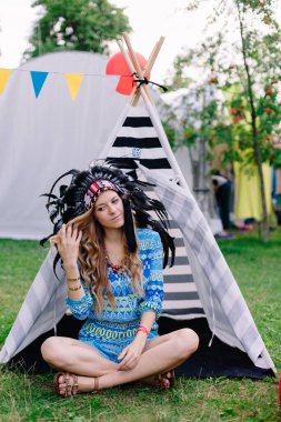 Şapkalı genç ve güzel bir bayan. Wigwam arka planında tüyleri var. Hakiki kızılderililer gibi. Yaz partisi.