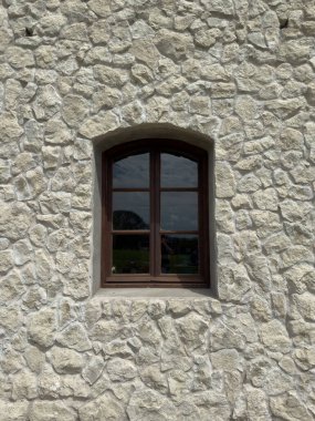 Geleneksel bir ahşap pencere desenli, pürüzlü taş bir duvara kurulmuş. Gökyüzü ve ağaçların yansımaları cam camlarda görünür..
