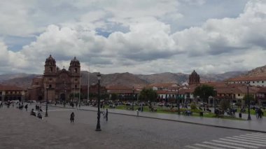 Parlak ve parçalı bulutlu bir günde Cusco, Peru 'daki Plaza de Armas' ın geniş bir görüntüsü. Meydan, arka planda sömürge binaları ve dağlarla çevrili Katedral yakınlarında yayalarla dolup taşıyor..