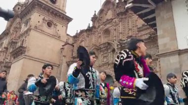Bir grup genç adam, geleneksel gümüş ve siyah halk dansları kostümleriyle bir halk festivali ya da halk festivali sırasında Plaza de Armas 'daki süslü Cusco Katedrali' nin önünde yürüyor ve gösteri yapıyorlar..