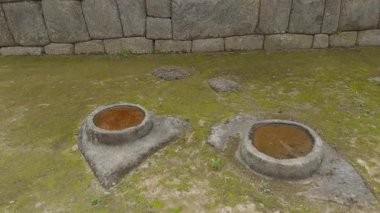 Çimenli bir alandaki iki dairesel taş merasim kuyusu ya da havan topu üzerine eğim atışı başlar ve ardından Machu Picchu 'daki ya da bağlantılı bir sitedeki mükemmel şekilde uyan gri İnka taş duvarını gözler önüne serer..