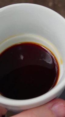 Beyaz seramik bardakta koyu, yeni demlenmiş koyu kahvenin yukarıdan aşağı görüntüsü, sıvı yüzeydeki ince yansımaları gösteriyor..