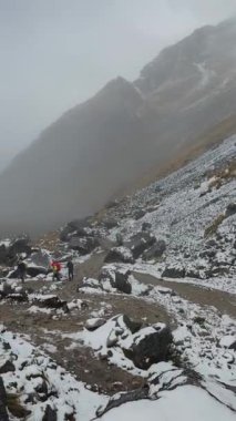Renkli sırt çantalı bir grup yürüyüşçü, And Dağları 'ndaki sisli bir günde kayalık ve karla kaplı bir patikada yol alırlar. Hava soğuk ve sisli..