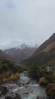 Soğuk bir dağ deresi ön plandaki kayaların üzerinden akar. Gözü karla kaplı büyük bir dağın zirvesine götürür. Kısmen bulutlar ve sis tarafından gizlenmiş ıssız bir yerde..